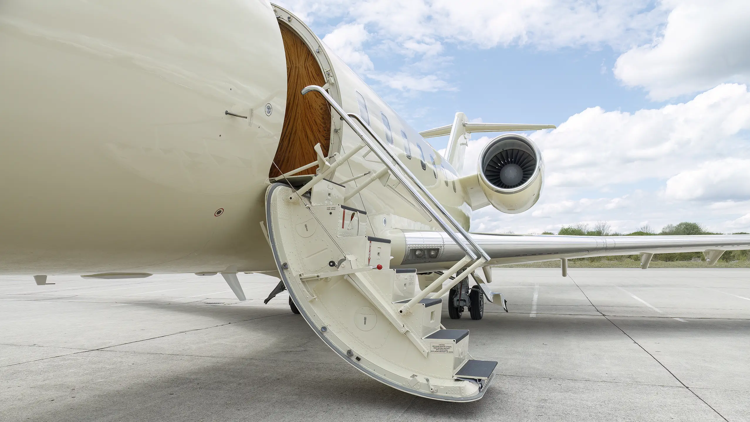 Close-up of an open private jet stairway leading into a cream-colored aircraft, with a visible engine and wing under a bright sky—ideal for showcasing Fly Airiness’ private jet charter services.
