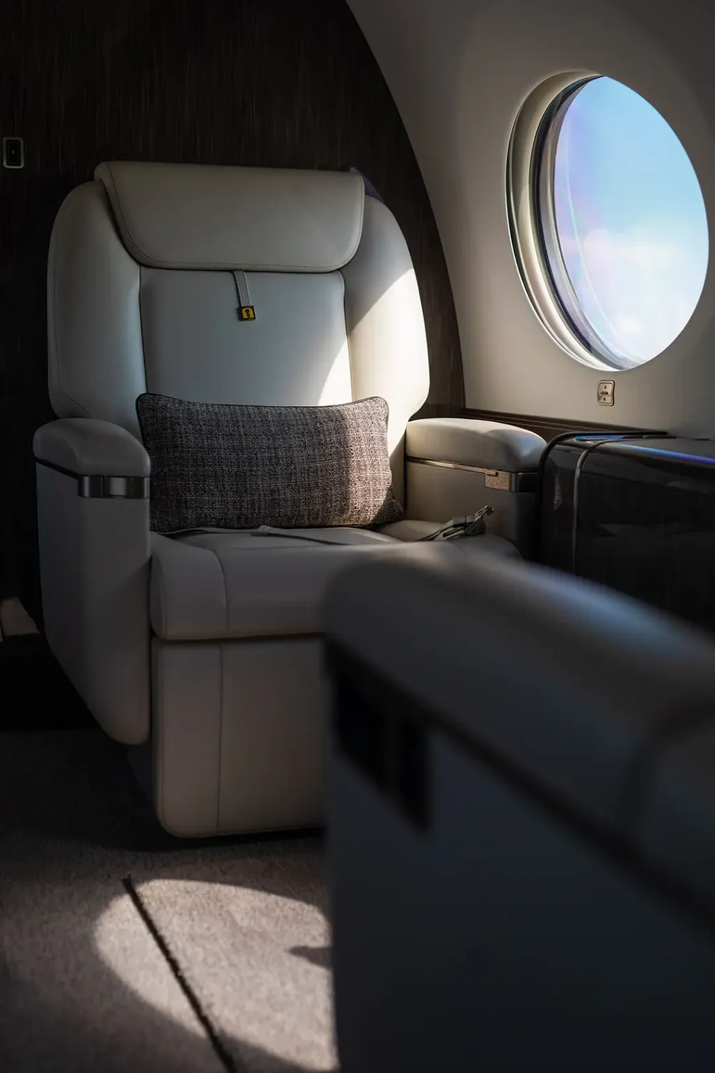 Luxurious leather seat with a textured pillow inside a private jet, lit softly by natural light through a nearby window. Captures the comfort and exclusivity central to high-end charter brokerage services.