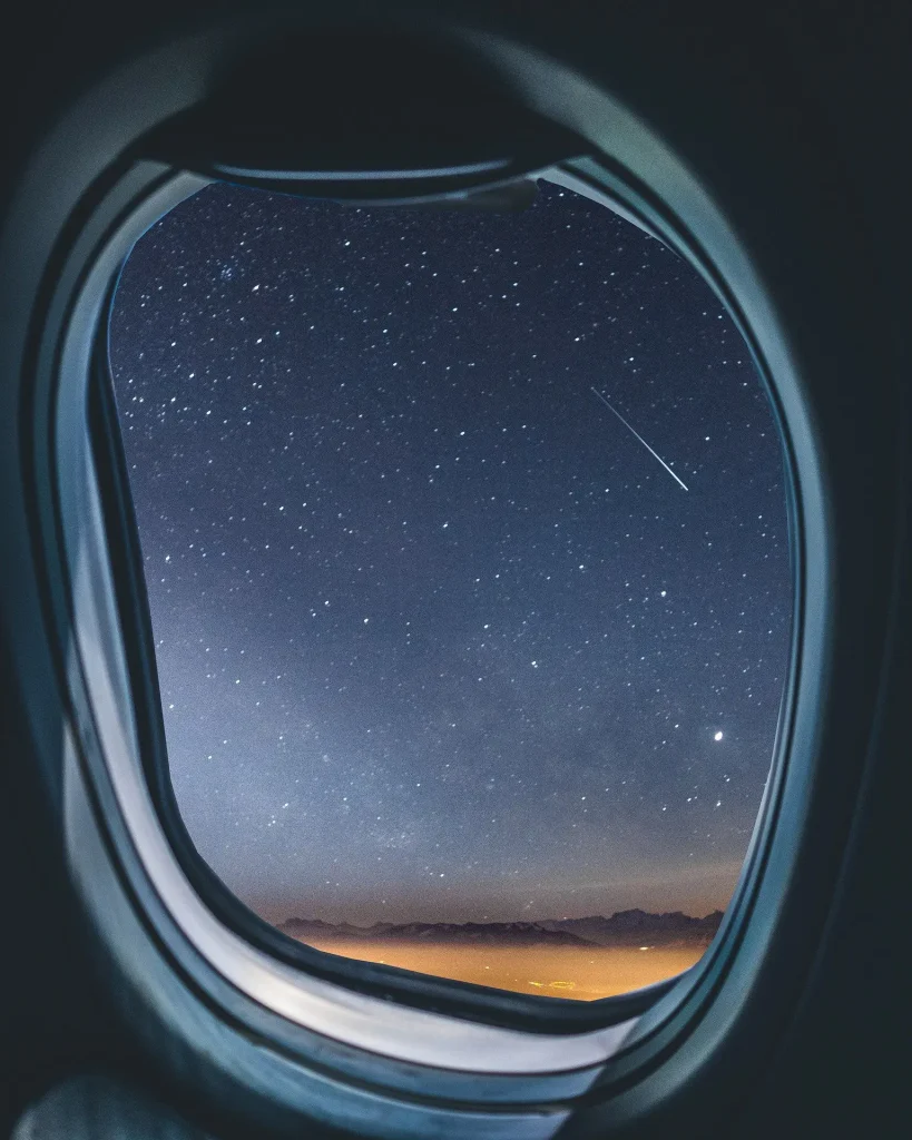 View from an airplane window at night showing a softly lit wing and deep blue sky, suggesting calm travel and professionalism. Ideal for an “About Us” page to convey experience, reliability, and a global perspective.